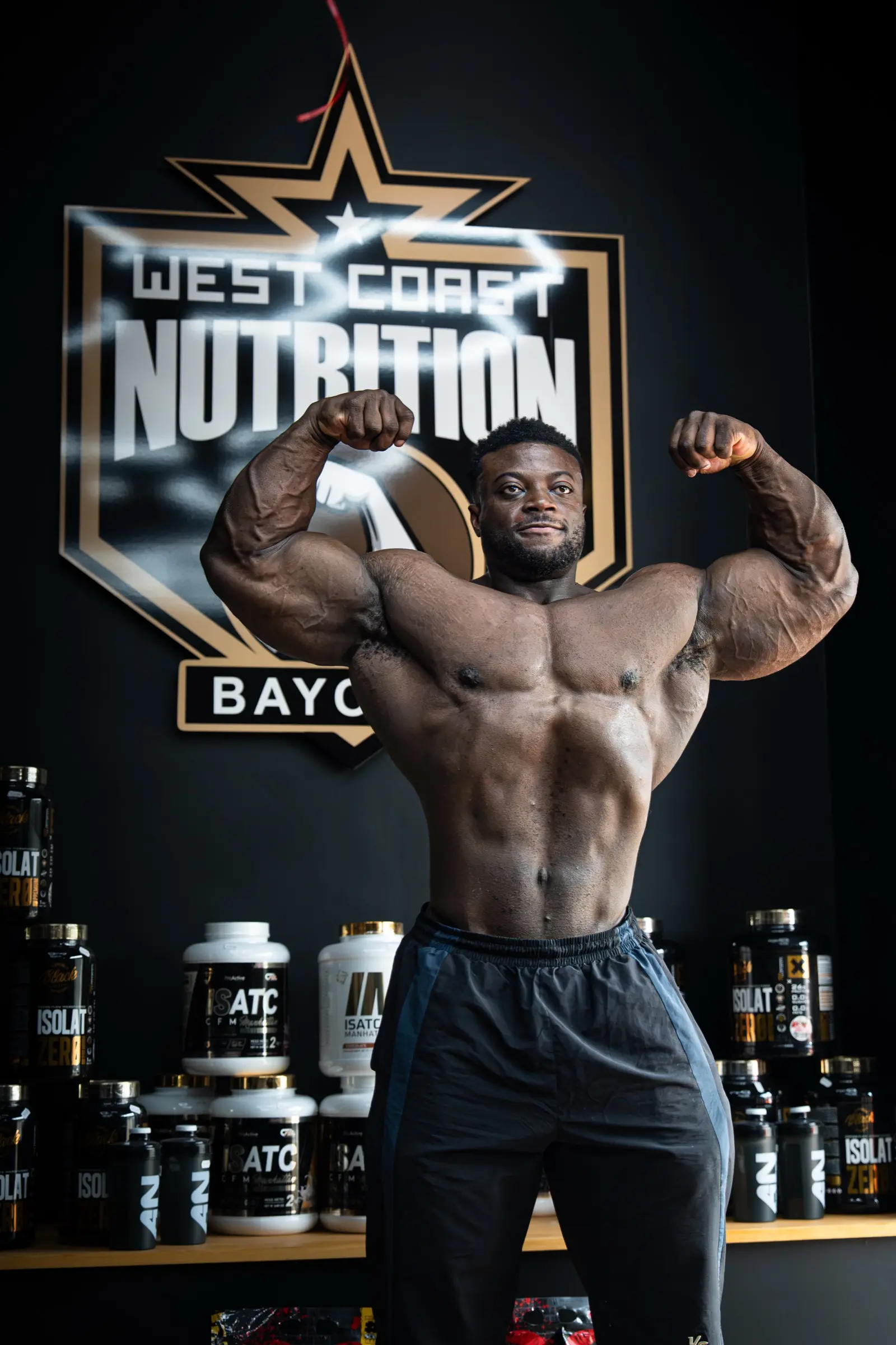 Bodybuilder en double biceps de face devant le logo West Coast Nutrition