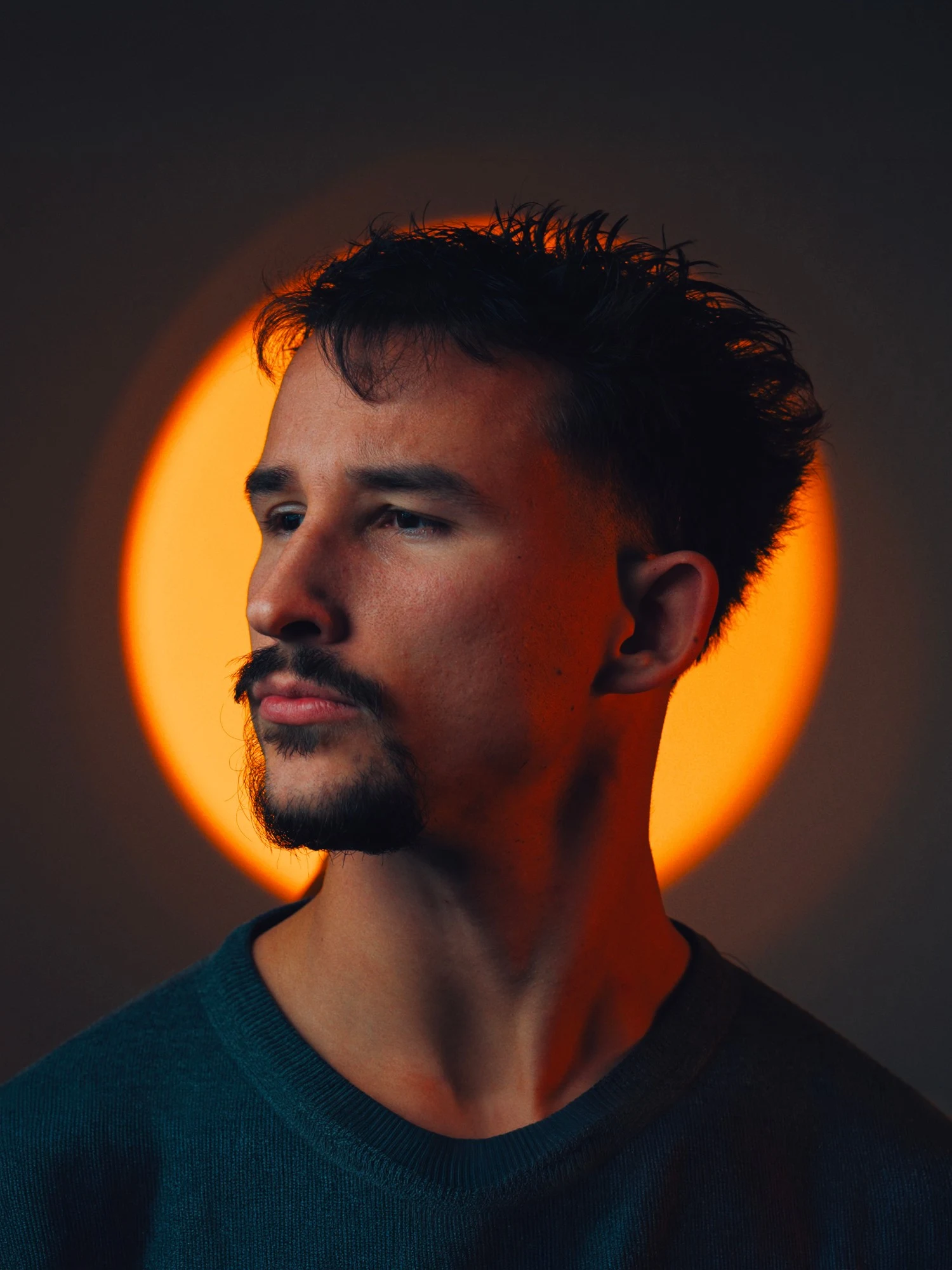 Portrait de Louka Belghazi, de trois quarts devant un halo de lumière orangée